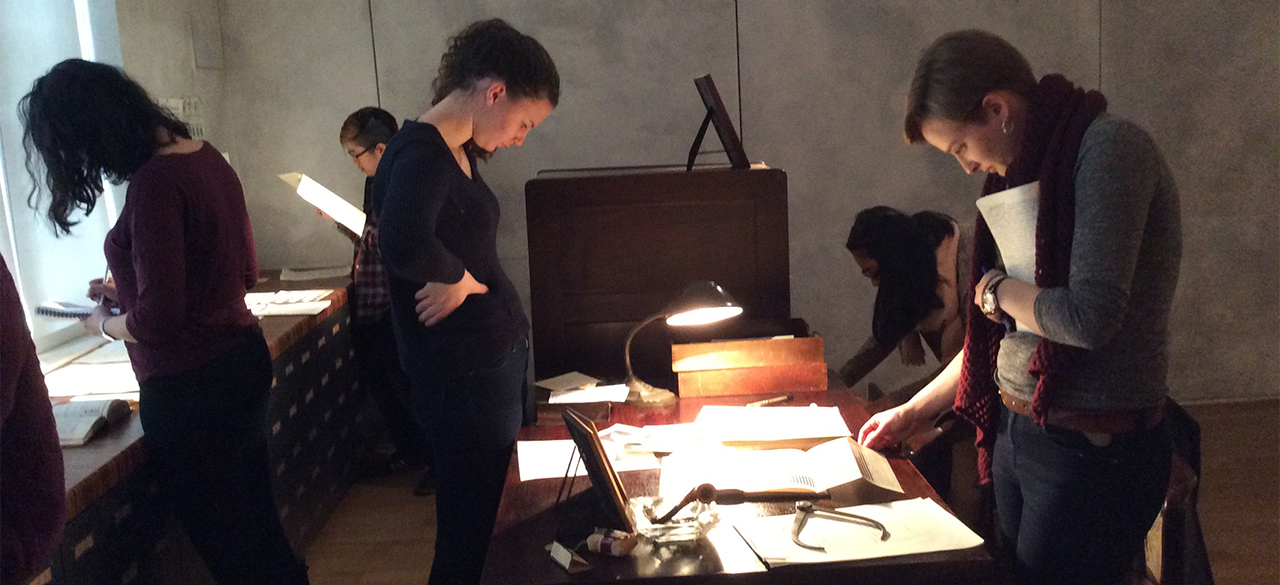 An Interdisciplinary Spring Seminar Married Theatre and Public Health. Students look at paper records spread across a table.