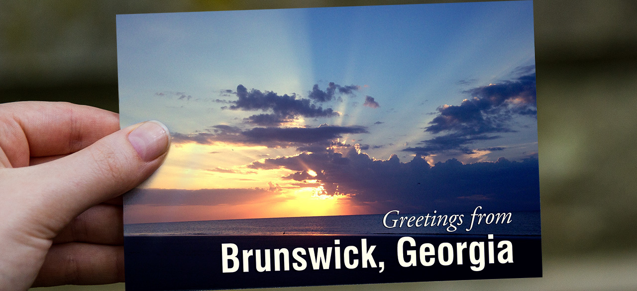 Hand holds a postcard that reads "Greetings from Brunswick, Georgia"