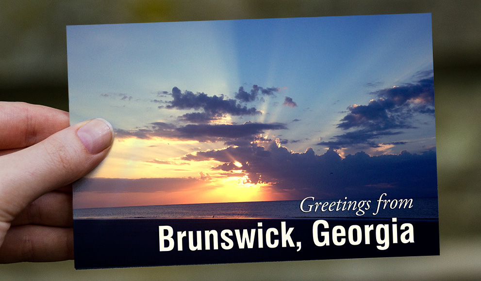 Hand holds a postcard that reads "Greetings from Brunswick, Georgia"
