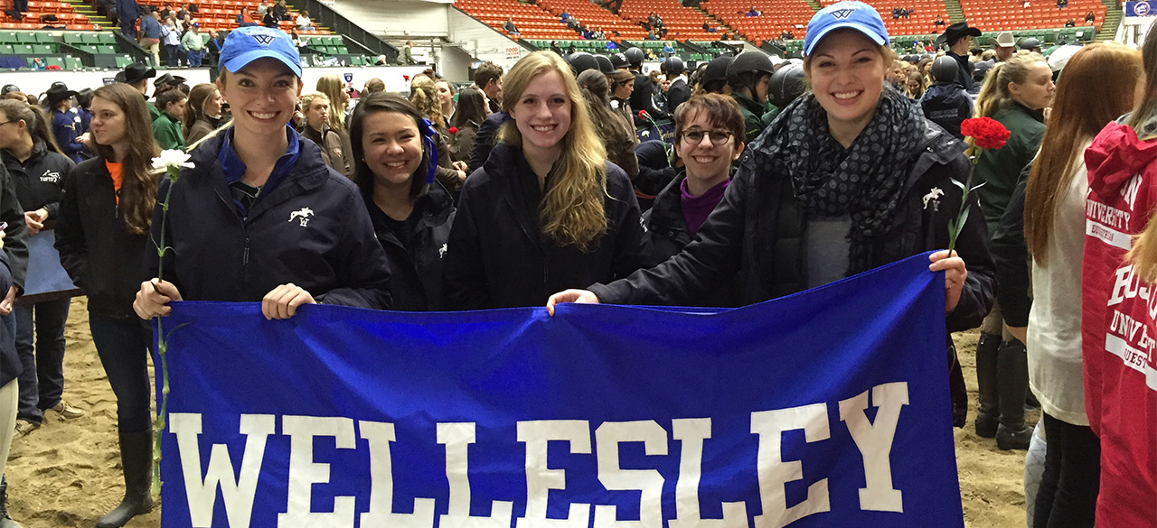 Equestrian team members hold a blue and white Wellesley Banner