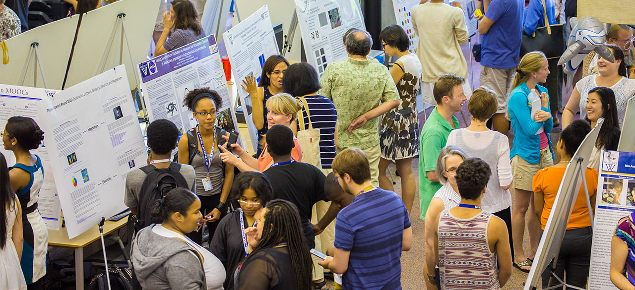 Poster Presentation Concludes Summer Research Program Students, faculty, and visitors gather around posters presenting student summer research.