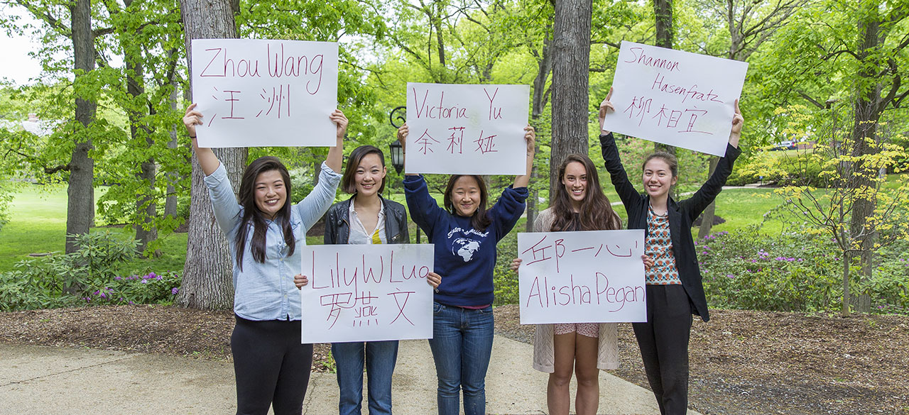 Diplomas to Include Names in Alternative Alphabets Students hold signs with their names written in English and an alternative alphabet.