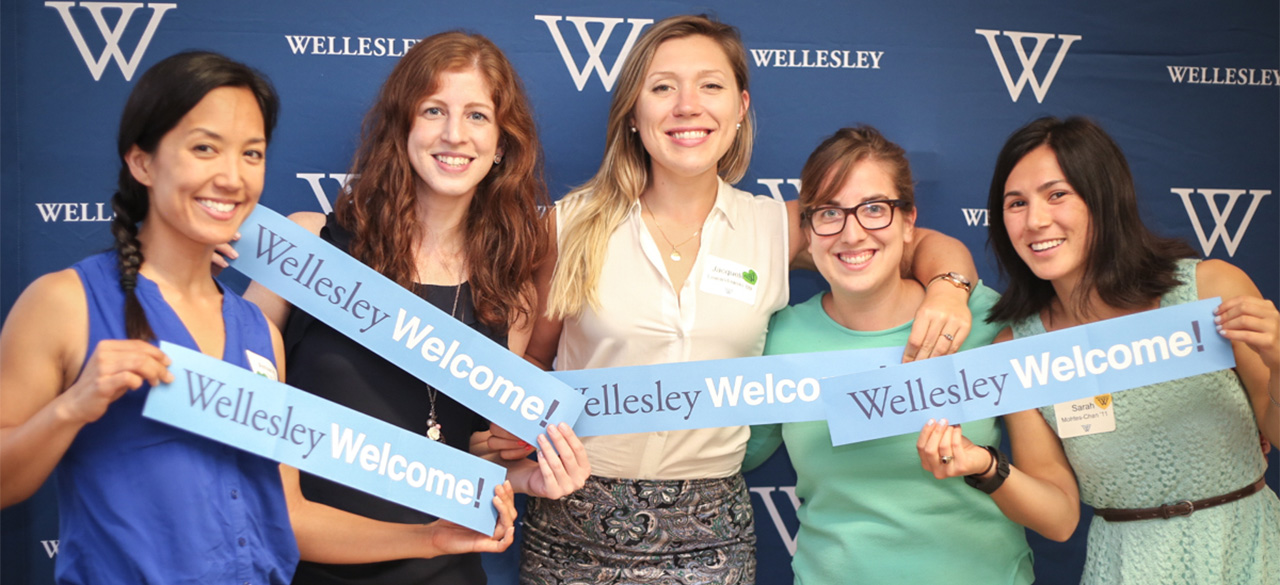Final Hours of the 2016 Participation Challenge Alumnae hold "Wellesley Welcome" signs in front of a blue backdrop