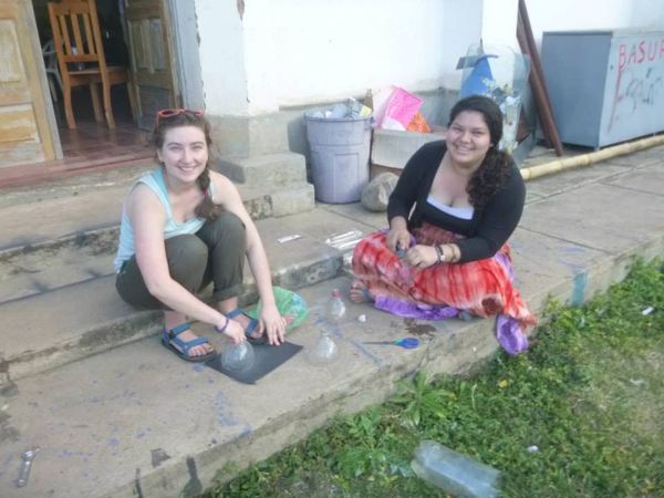 Two Wellesley students smiling at the camera as they work on modifying plastic bottles while sitting on concrete steps