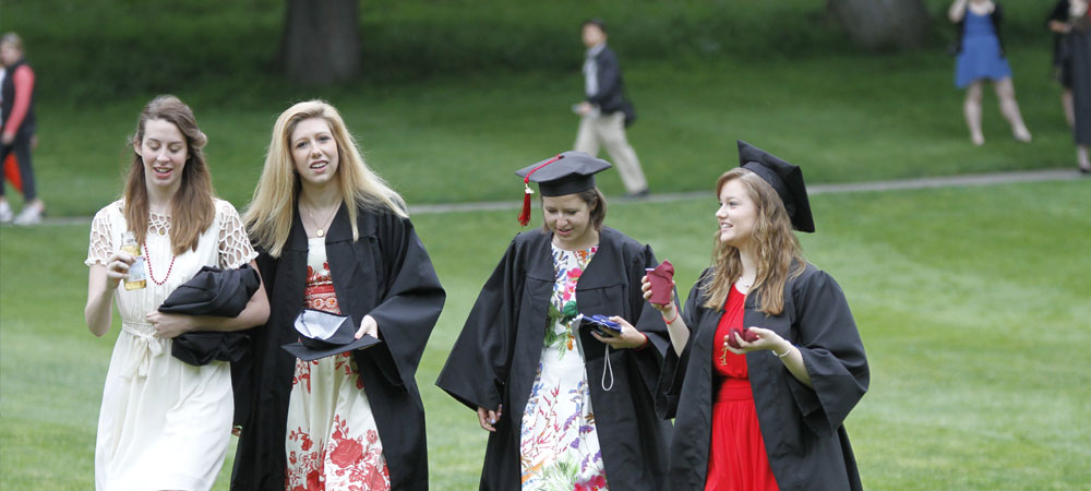 Four students wearing robes walk across Severance Green