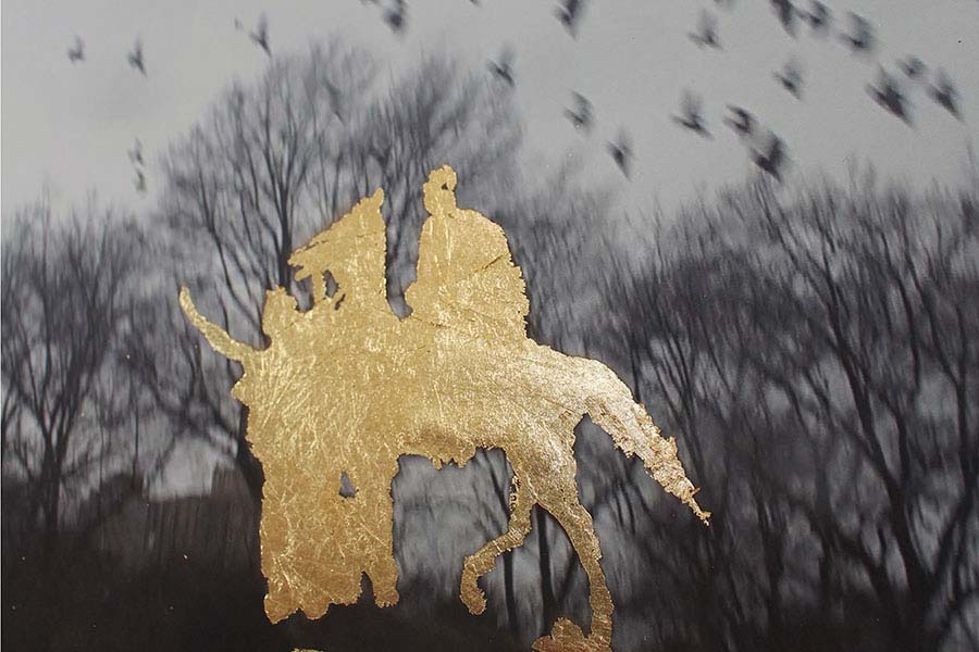 abstract gold silhouette seemingly of a person on a horse set against a black and white photograph of birds flying above trees