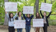 Diplomas to Include Names in Alternative Alphabets Students hold signs with their names written in English and an alternative alphabet.