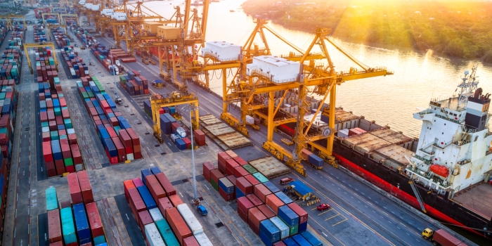Wellesley Economist Says U.S. Foreign Direct Investment Is a Casualty of the Trade War Logistics and transportation of Container Cargo ship with working crane bridge in shipyard at sunrise,