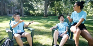 Wellesley Student Leaders Take an End of Summer Break to Enjoy Nature Three students sit at the Academic Quad in Adirondack Chairs, talking.