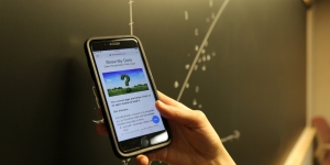 Wellesley Professor’s Data Visualization App Helps Users Create Compelling Graphs A close shot of someone holding a phone that reads "show my data" in front of a blackboard with the scatter plot.