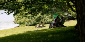 Student Art Project Celebrates Geographical Interconnections Two people sit by lake waban near signs that read the names of cities around the world.