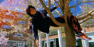Senior Snapshot, Sophia Peña ’22: “Think Critically About the Science You’re Producing” A student sits in the base of a tree with one hand grasping a branch and the other dangling behind her. She smiles at the camera