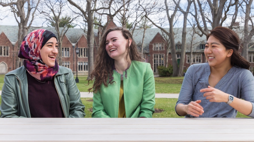 Three student sit in the academic quad in conversation. 