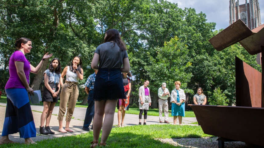 A student describes a sculpture in the academic quad