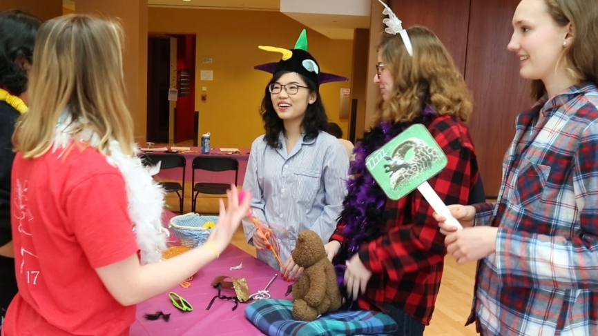Students stand around a table with dress up props on it.