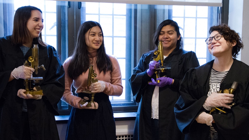 Four students stand in President Johnson's office, holding microscopes and chatting.