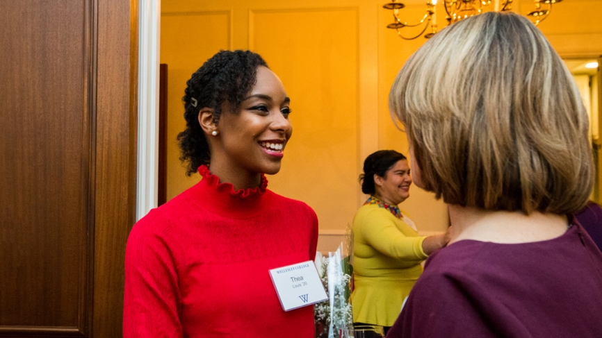 A student in a red sweater talks to another woman with her back to the camera