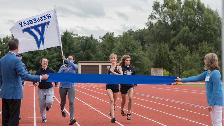 Students run on the track for the first time while carrying a Wellesley flag.