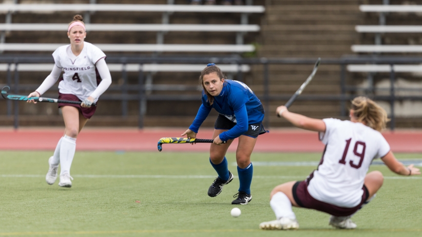 A Wellesley field hockey player prepares to pass a ball around two players from the opposite team.