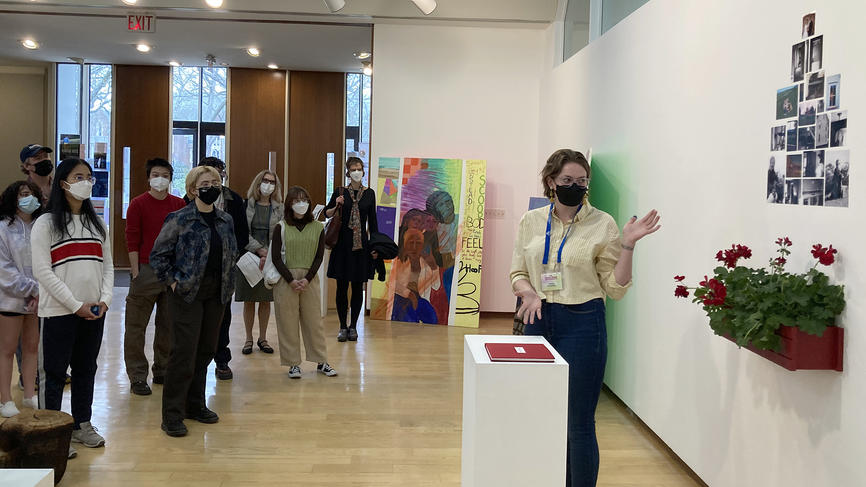 Grace Ramsdell ’22 gestures to photos on the wall behind her while an audience looks on.