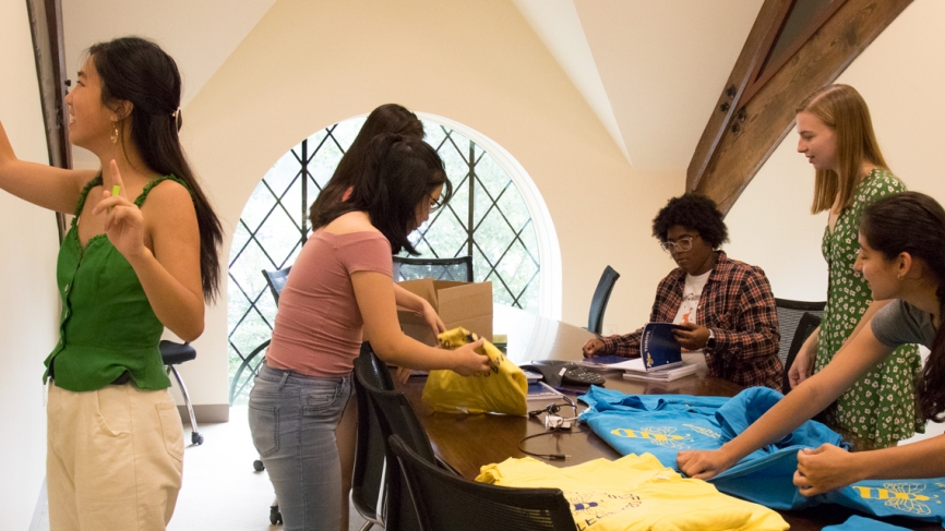 Six students fold t shirts in an office space.