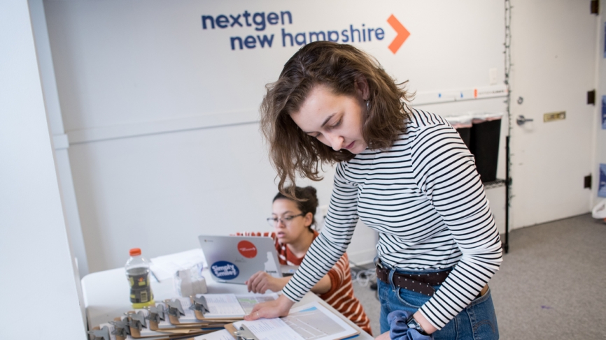 a woman looks down at a series of clipboards on a table. behind her a table reads, nextgen america