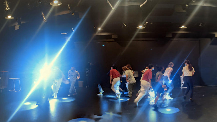 people practicing theater in a dark room with a bright spotlight