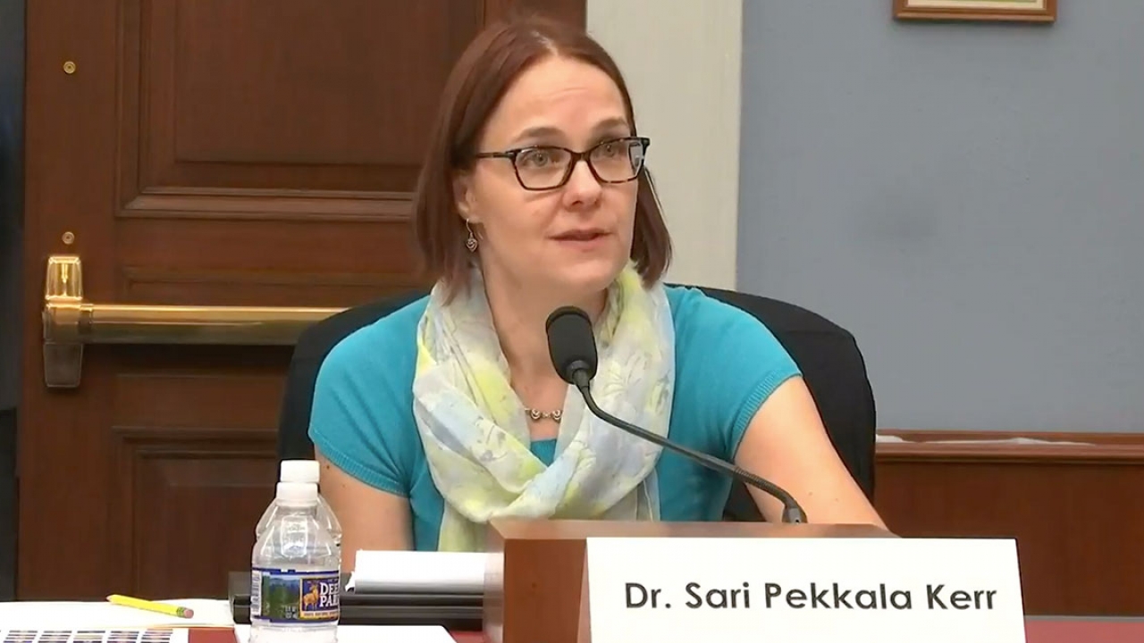 A woman sits at a table with a microphone.