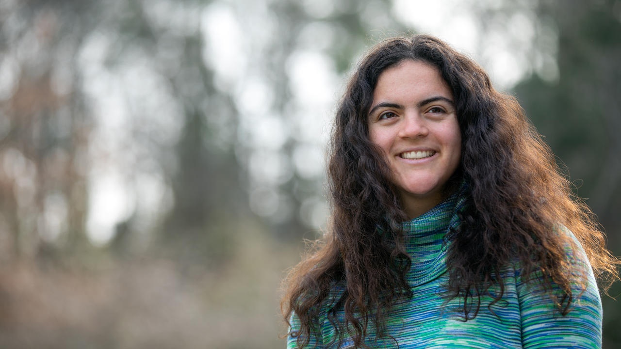 A woman poses outside in a teal sweater