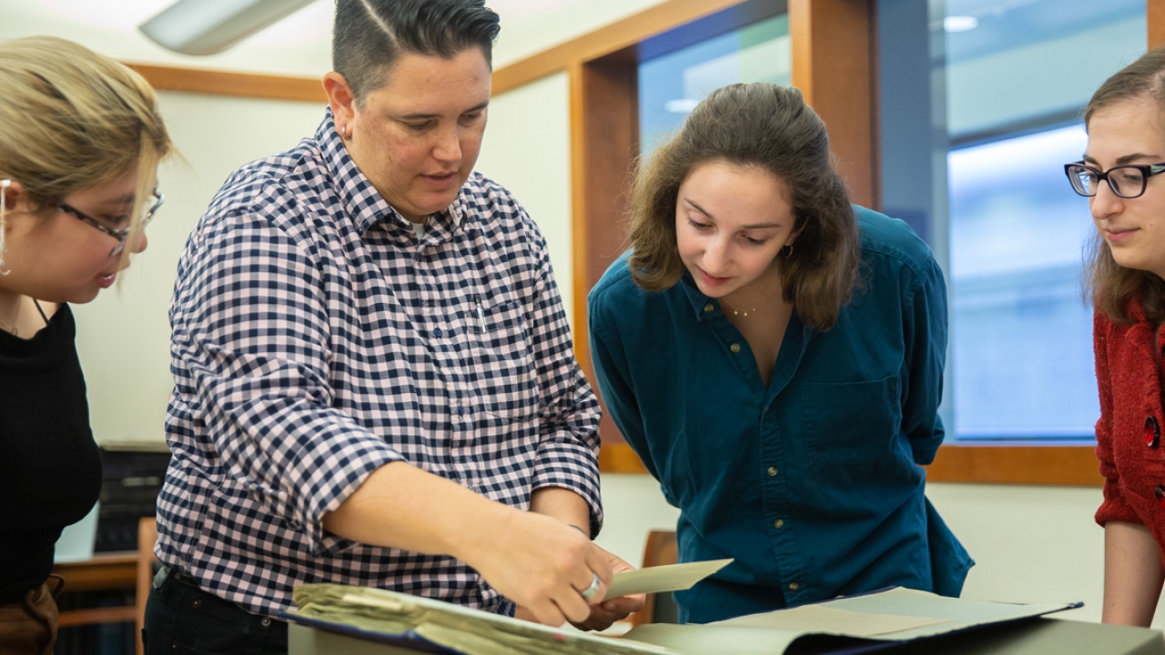 Wellesley College archivists talk with students in the archives. They look at a book.  