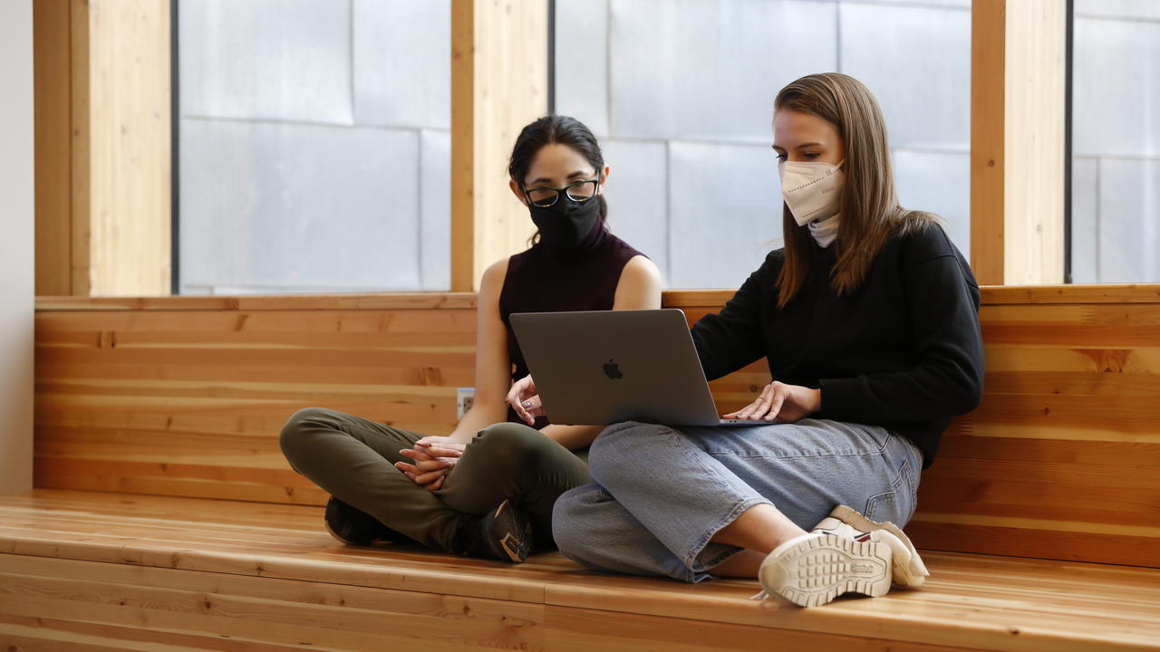 two students sit together looking at a laptop