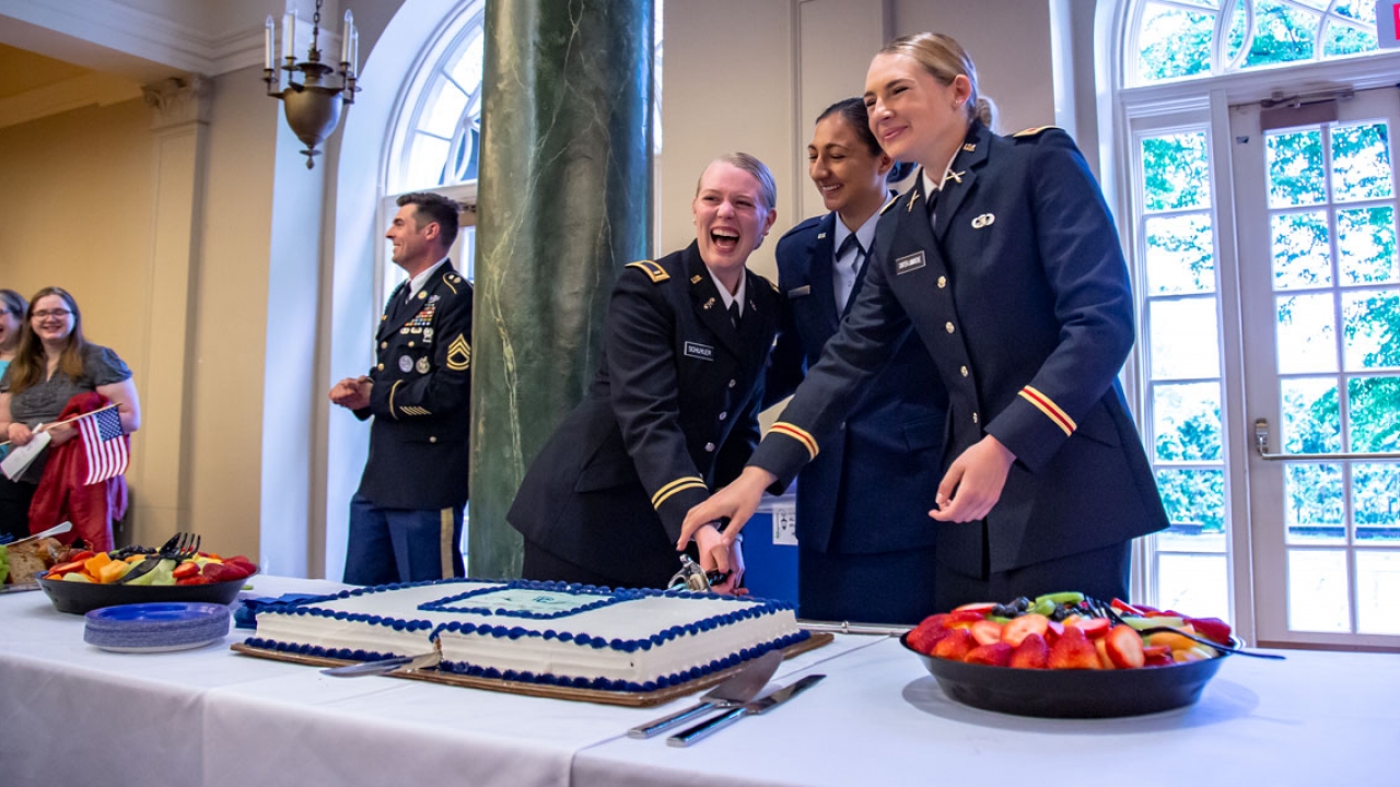 Three ROTC cadets cut a cake with a saber