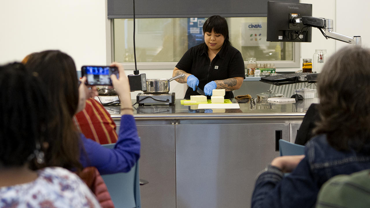Bettina Makalintal ’14 cuts tofu in front of an audience in the cooking lab. 