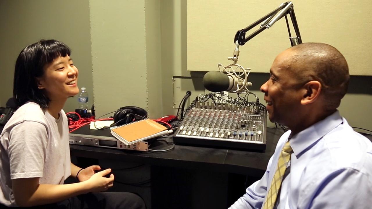 A student and staff member sit in a recording studio, talking.