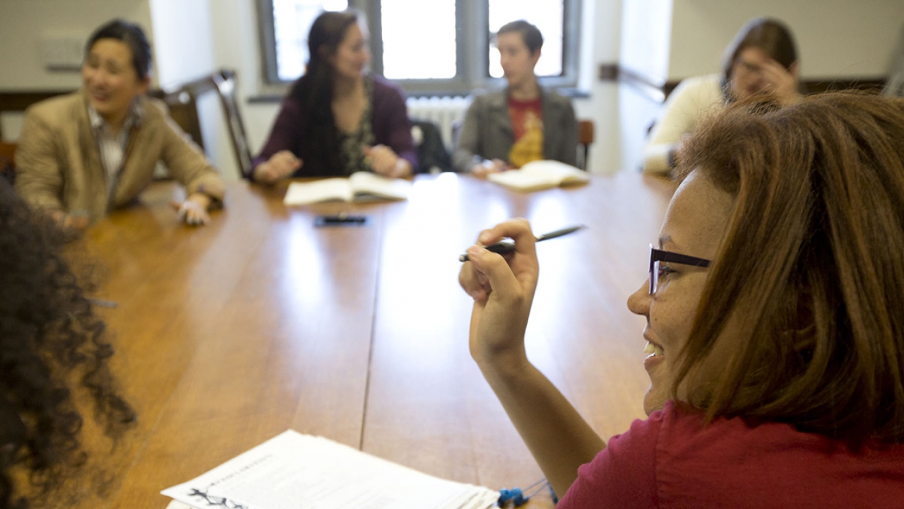 A group os students sit around a large, wooden table, talking to one another in a Calderwood Seminar.