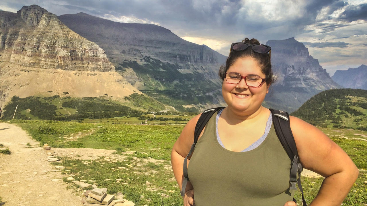Photo of a woman looking at the camera smiling. There are mountains behind her.