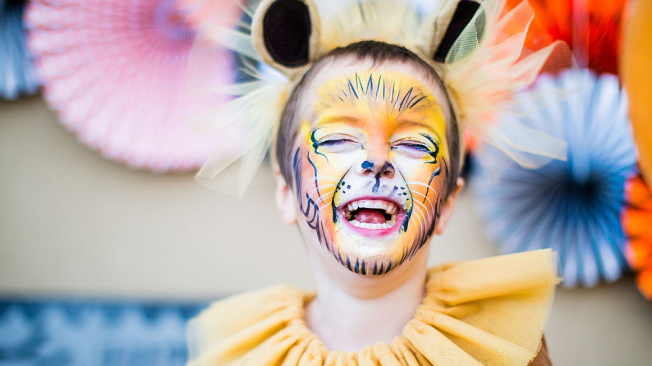 A child dressed up as a lion. He laughs.