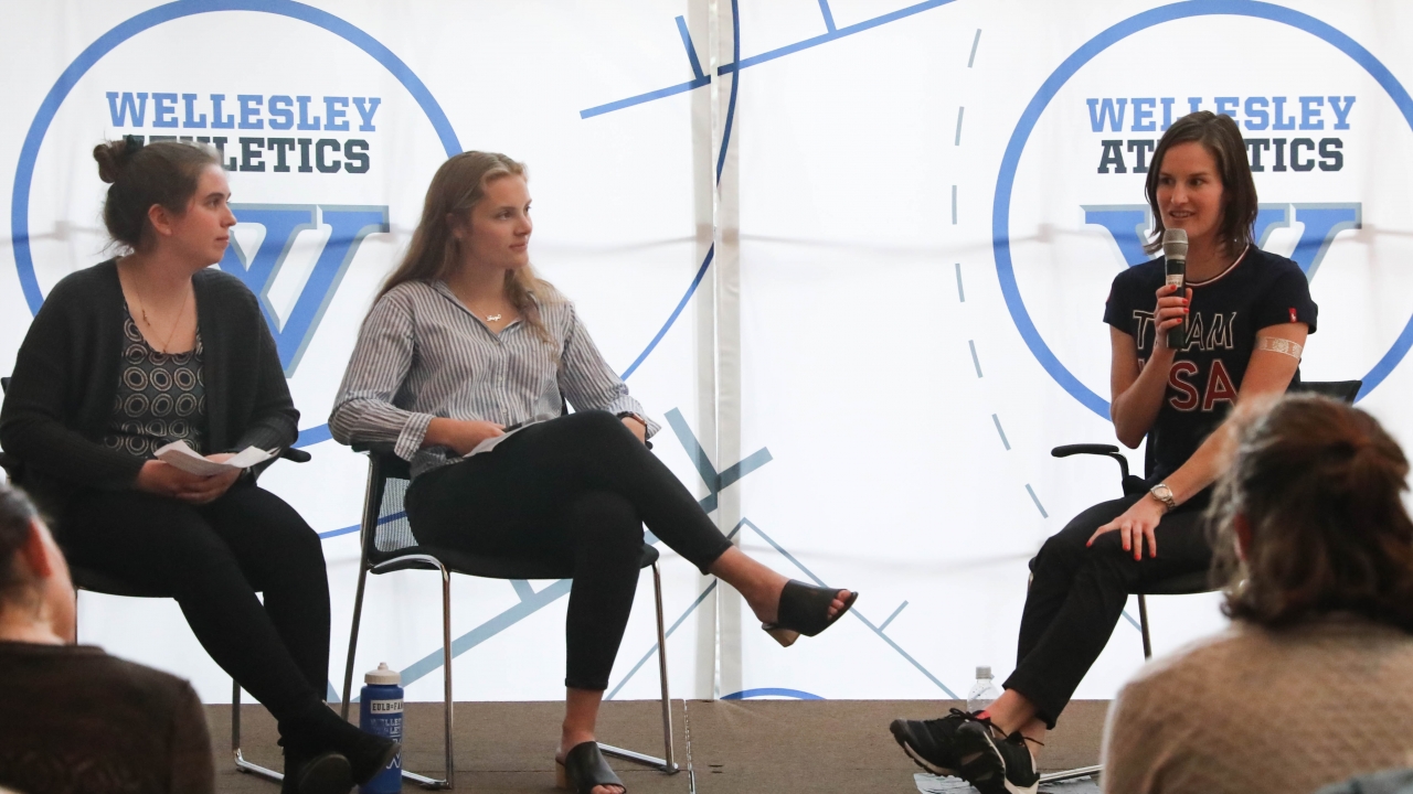 Clare Egan sits with two students talk to a crowd of people.