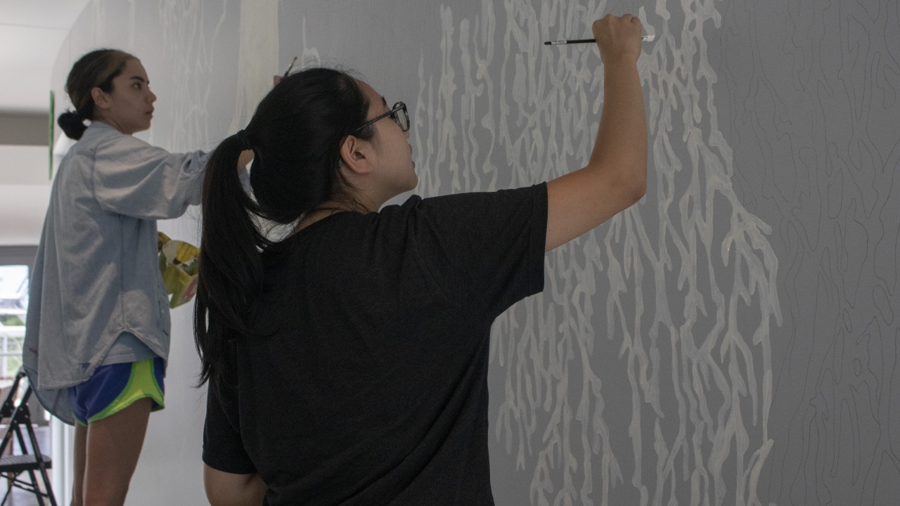 Two students work on a walled mural.