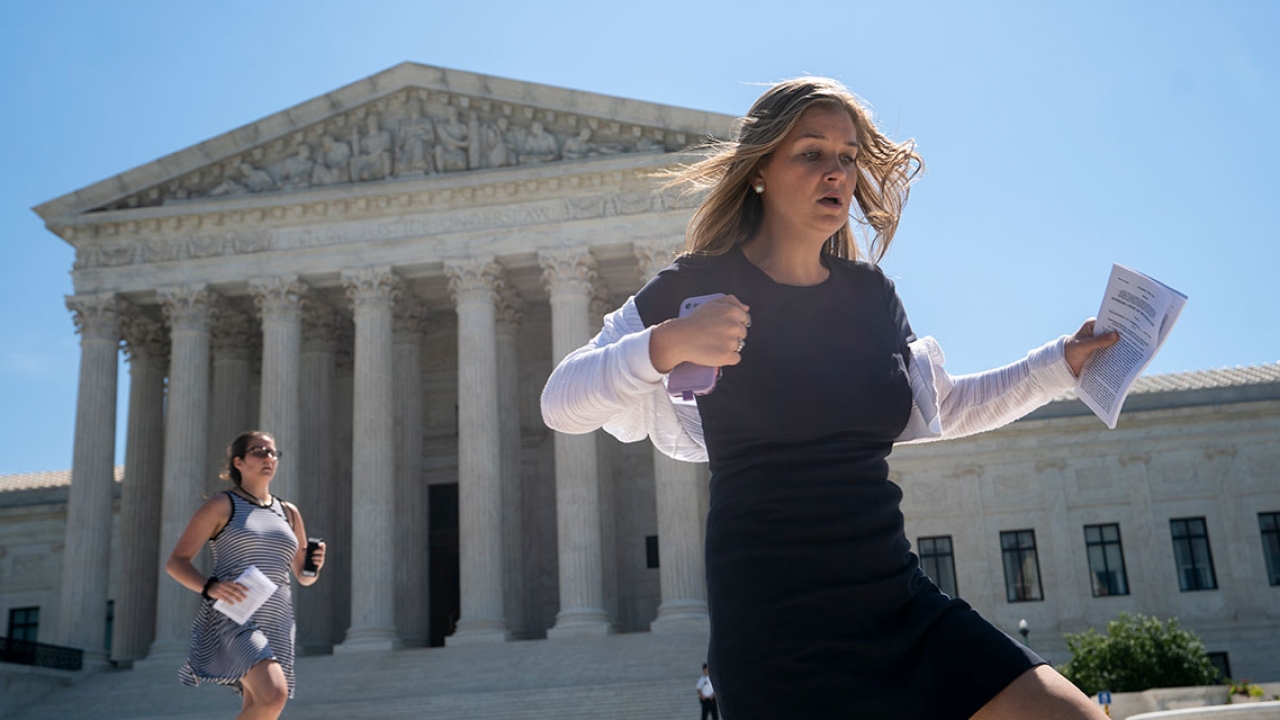 Two aids sprint down the steps of the Supreme Court holding decisions.